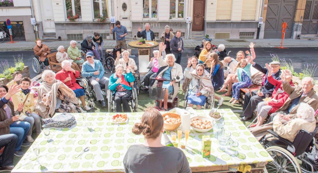 Groep ouderlingen rond een grote tafel op straat